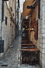 a narrow alleyway with tables and umbrellas