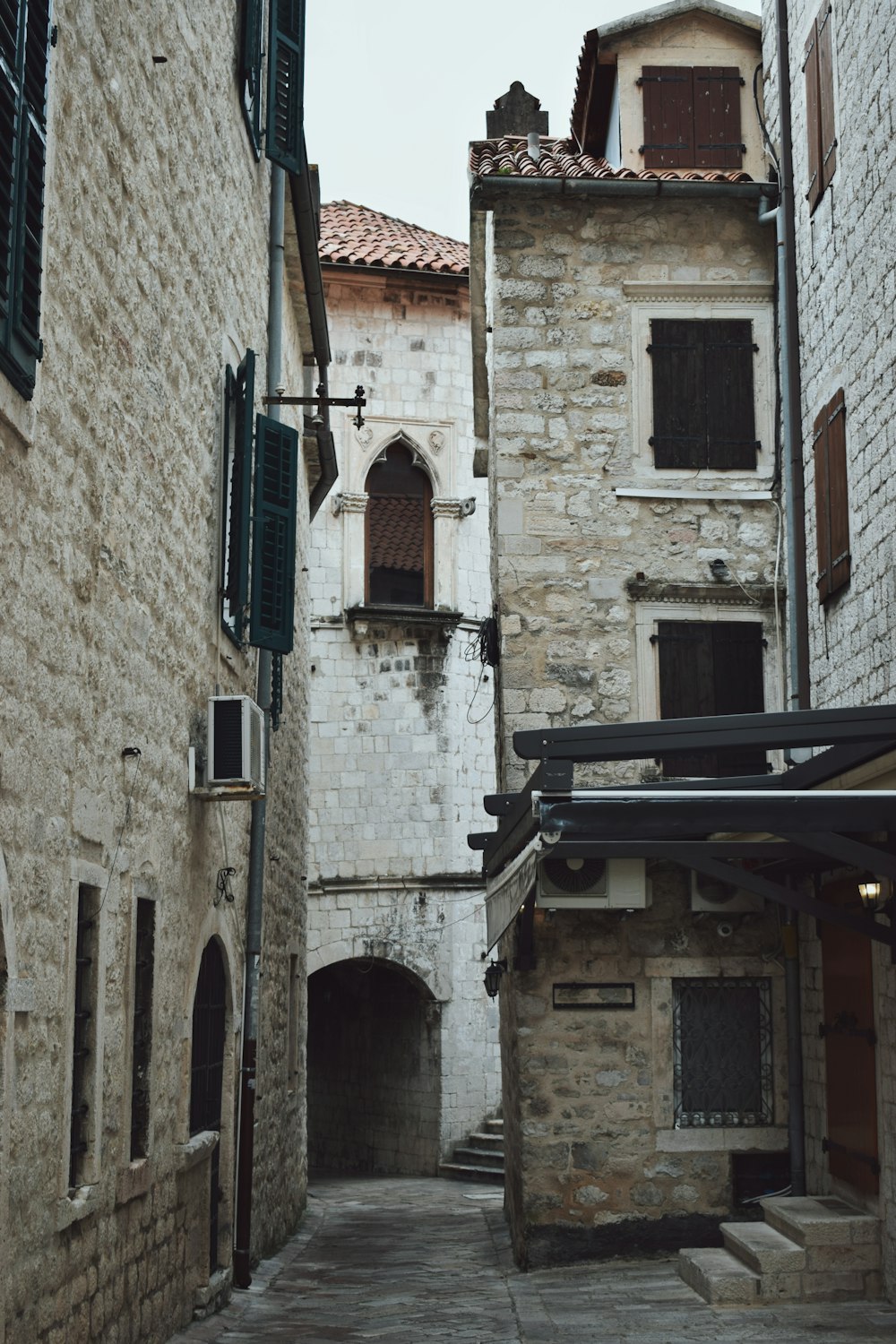 a narrow alley way with stone buildings and green shutters