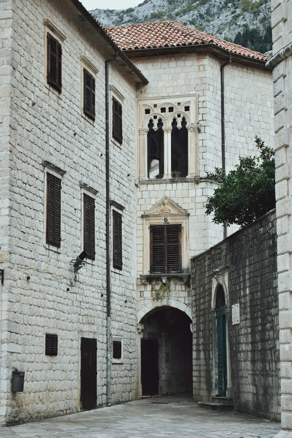 A Gothic-Renaissance stone palazzo in Kotor's Old Town, with the fortress-topped mountain rising behind it
