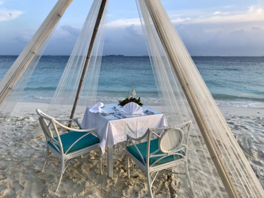 A romantic candlelight dinner setup on a sandy beach at sunset.