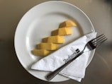 Slices of yellow mango are neatly arranged on a white plate. A silver fork rests on a white napkin, which is placed on the plate, featuring the Radisson Blu logo.