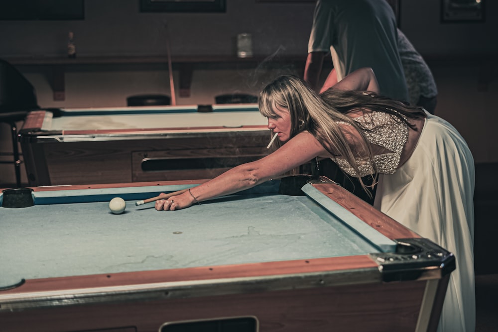 a woman leaning over a pool table to hit a ball