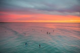 A vibrant shot of surfers catching waves under a neon-lit sunset at Penang beach.