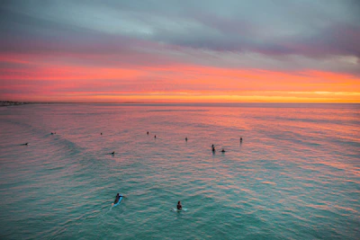 A vibrant surf camp beachfront with colorful houses and surfers catching waves at sunset.