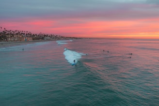 A dynamic shot of surfers catching waves under a neon-lit sunset at Penang beach.