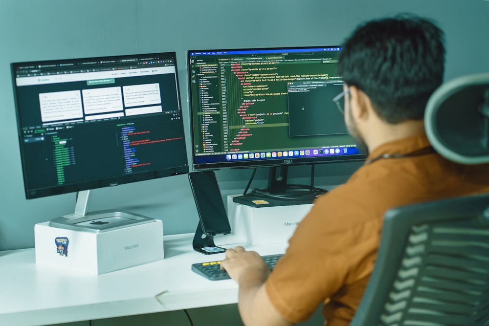 a man sitting in front of two computer monitors