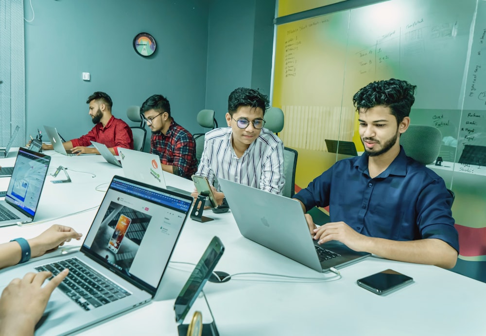 a group of people sitting around a table with laptops