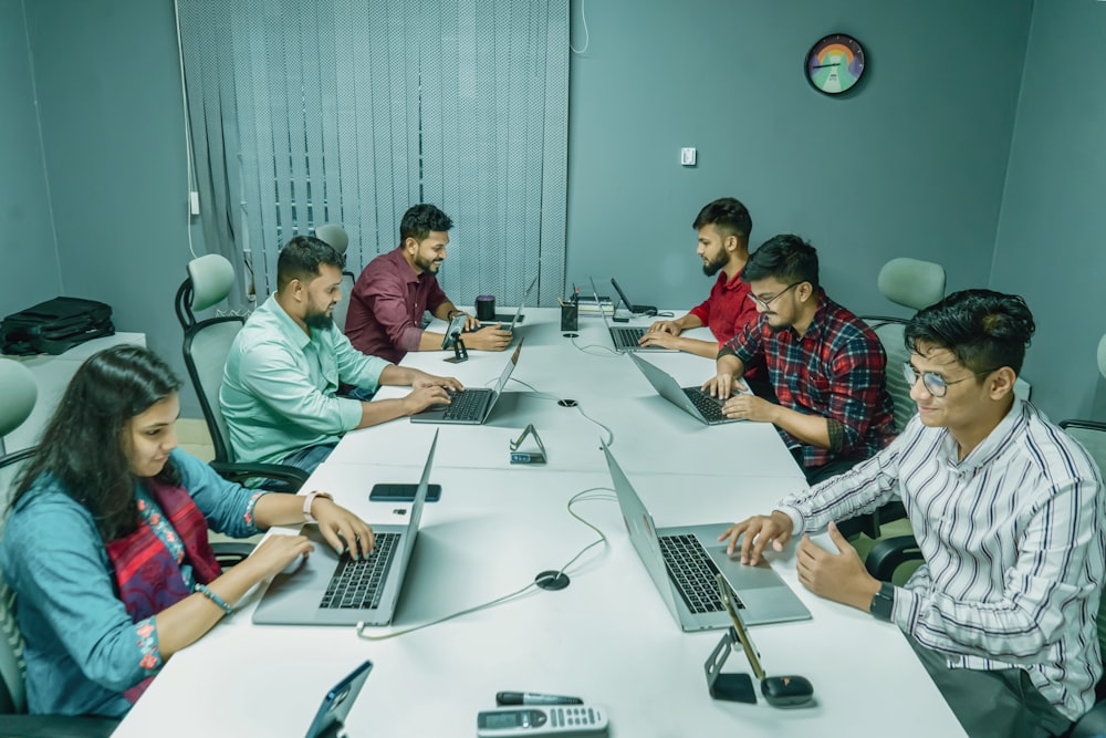 um grupo de pessoas sentadas ao redor de uma mesa com laptops