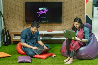 a man and a woman sitting on bean bag chairs looking at a laptop