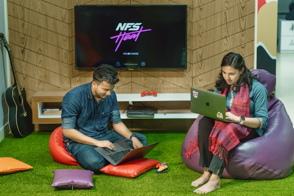 a man and a woman sitting on bean bag chairs looking at a laptop