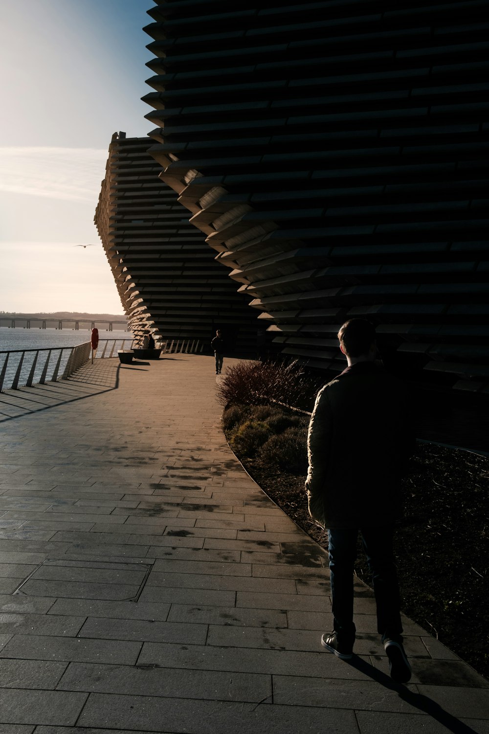 a man standing on a sidewalk next to a body of water