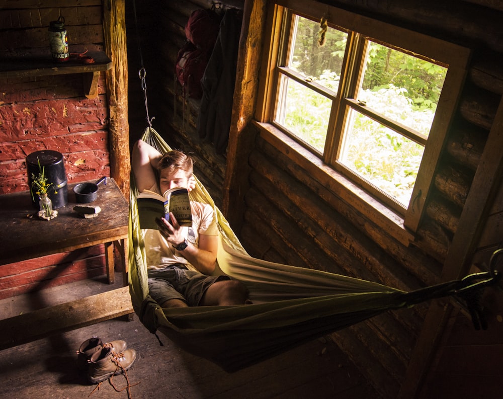 a man laying in a hammock reading a book