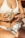 A person wearing a white bikini is holding a large glass filled with a clear drink, garnished with lemon slices and a sprig of rosemary. The person has colorful painted nails and a tattoo on their arm. A bottle of liquor labeled 'SEXO ABSINTO' rests on their lap.
