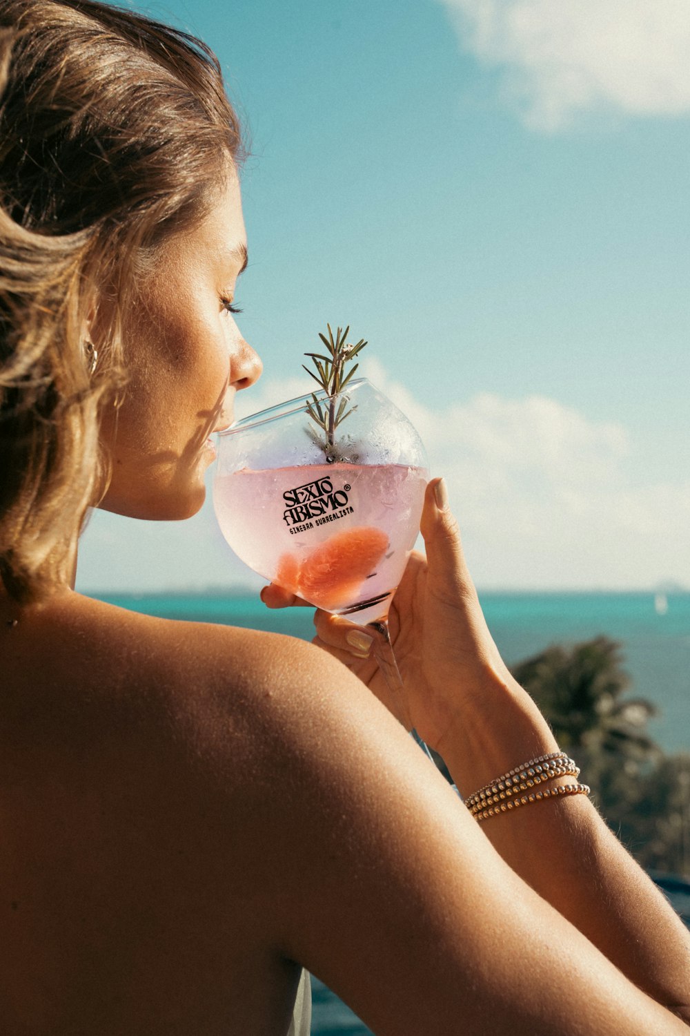 a woman drinking a drink with a view of the ocean