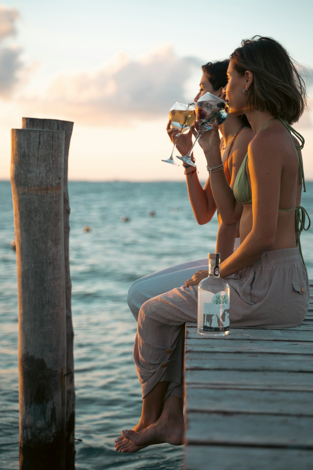 two women sitting on a dock drinking wine