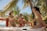 Three women in swimsuits are enjoying drinks while sitting in a hot tub surrounded by lush palm trees. The setting appears to be tropical, with clear blue skies and a wooden deck nearby.