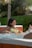 Smiling woman relaxing beside a sparkling clean outdoor jacuzzi in a cozy garden setting.