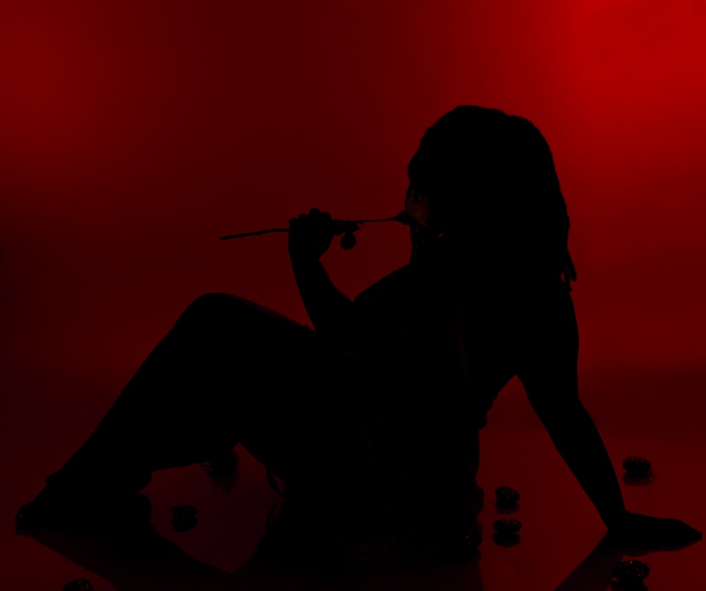 a silhouette of a woman sitting on the ground with a cigarette in her mouth