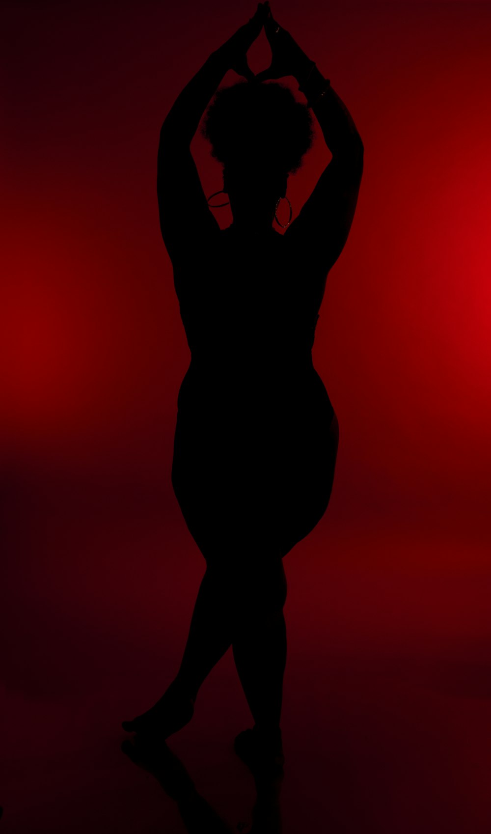 a silhouette of a woman doing yoga in front of a red background