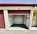 A storage unit with a partially open red roll-up door. The interior is empty, showing metallic wall panels with some insulation visible at the sides. The building has a cream color with a small label 'F-8' above the entrance.