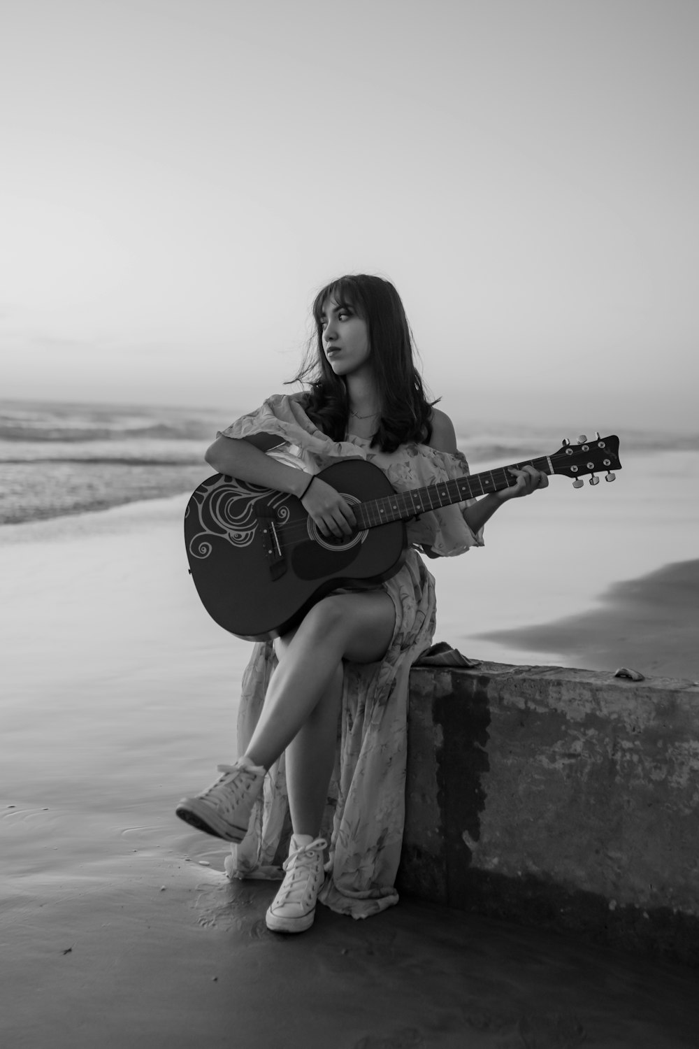 a woman sitting on a wall playing a guitar