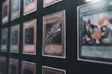 Several collectible cards are displayed in a grid-like pattern within a frame. One prominent card in the foreground features a dragon motif and is labeled 'Curse of Dragon.' The cards are in protective sleeves, and the display appears to be a part of a larger collection.