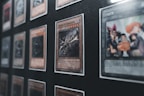 Several collectible cards are displayed in a grid-like pattern within a frame. One prominent card in the foreground features a dragon motif and is labeled 'Curse of Dragon.' The cards are in protective sleeves, and the display appears to be a part of a larger collection.