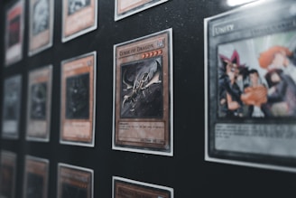 Several collectible cards are displayed in a grid-like pattern within a frame. One prominent card in the foreground features a dragon motif and is labeled 'Curse of Dragon.' The cards are in protective sleeves, and the display appears to be a part of a larger collection.