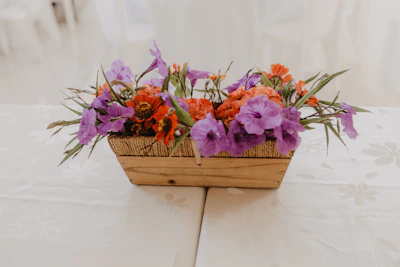A woven decorative basket filled with fresh flowers on a rustic wooden floor.
