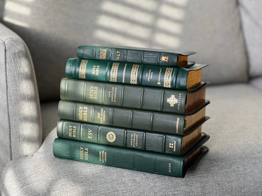 A collection of beautifully bound Bibles with golden edges stacked on a wooden table bathed in soft morning light.