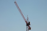 A towering steel gray tower crane silhouetted against a clear blue sky.