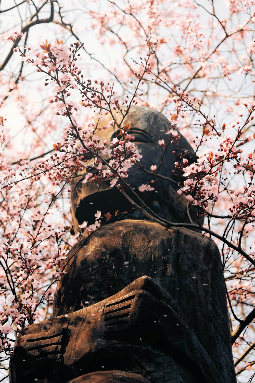 a statue in the middle of a tree with pink flowers