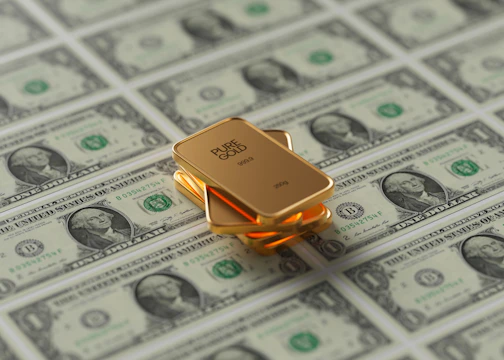 Gold bars are stacked on a surface covered with one-dollar bills. The gold bars have a reflective and polished surface, indicating purity and value.