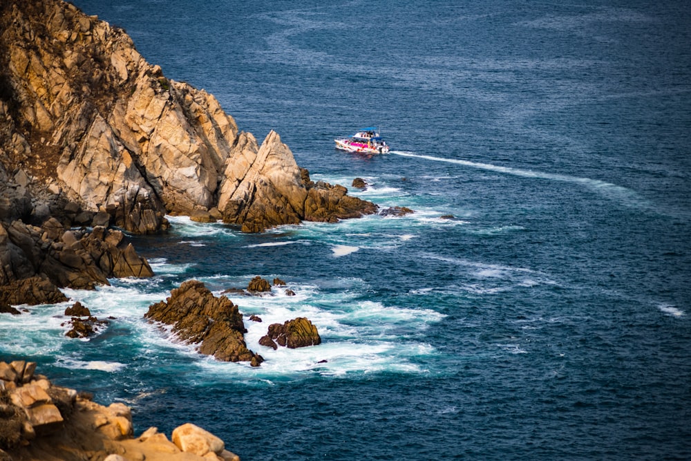 a boat traveling through the ocean next to a rocky shore