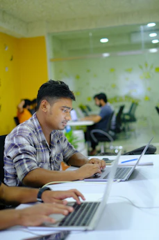A diverse group of tech professionals collaborating over laptops in a bright, modern workspace.