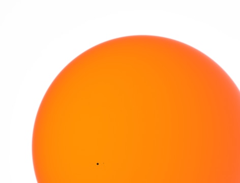 A large, bright orange circle dominates the image against a white background. A small black dot is visible near the bottom edge of the circle.