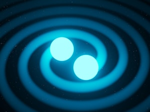 Two glowing blue spheres are positioned centrally, surrounded by circular ripples expanding outward on a dark background. The image has a cosmic or scientific theme, possibly representing gravitational waves or a similar astronomical phenomenon.