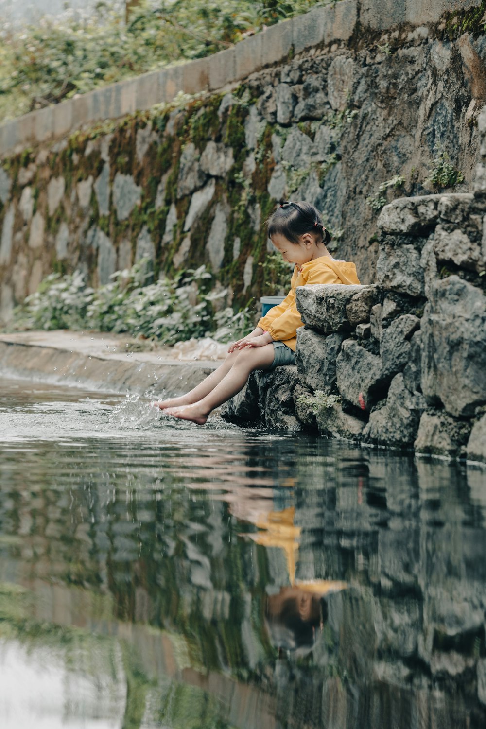 a young boy sitting on a rock next to a body of water
