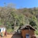 A rural setting with a thatched-roof hut and a solar panel in the foreground, surrounded by lush greenery and hills. A woman and a child are seen interacting, while another person stands near the hut, engaging in daily chores under a clear blue sky.