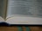 An open book displaying a page with text in columns. The paper appears slightly yellowed, indicating age, and there is a green bookmark ribbon visible at the bottom.