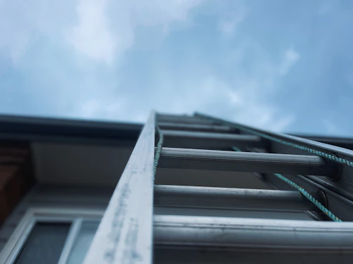 A sleek expandable aluminium ladder extended to full height outdoors on a sunny day.