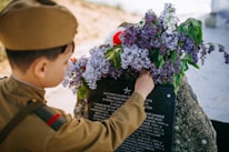 Close-up of a hand placing a flower on a memorial stone engraved with a heartfelt message.