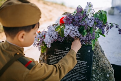 Close-up of a hand placing a flower on a memorial stone engraved with a heartfelt message.