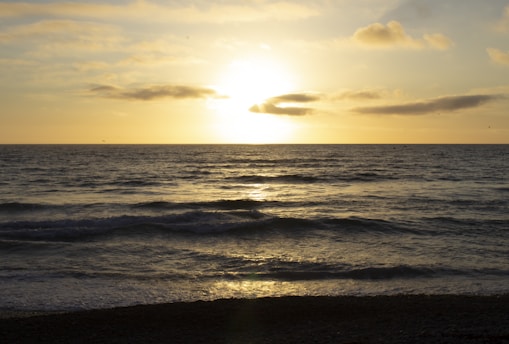 A serene ocean horizon at sunrise with gentle waves reflecting soft golden light.