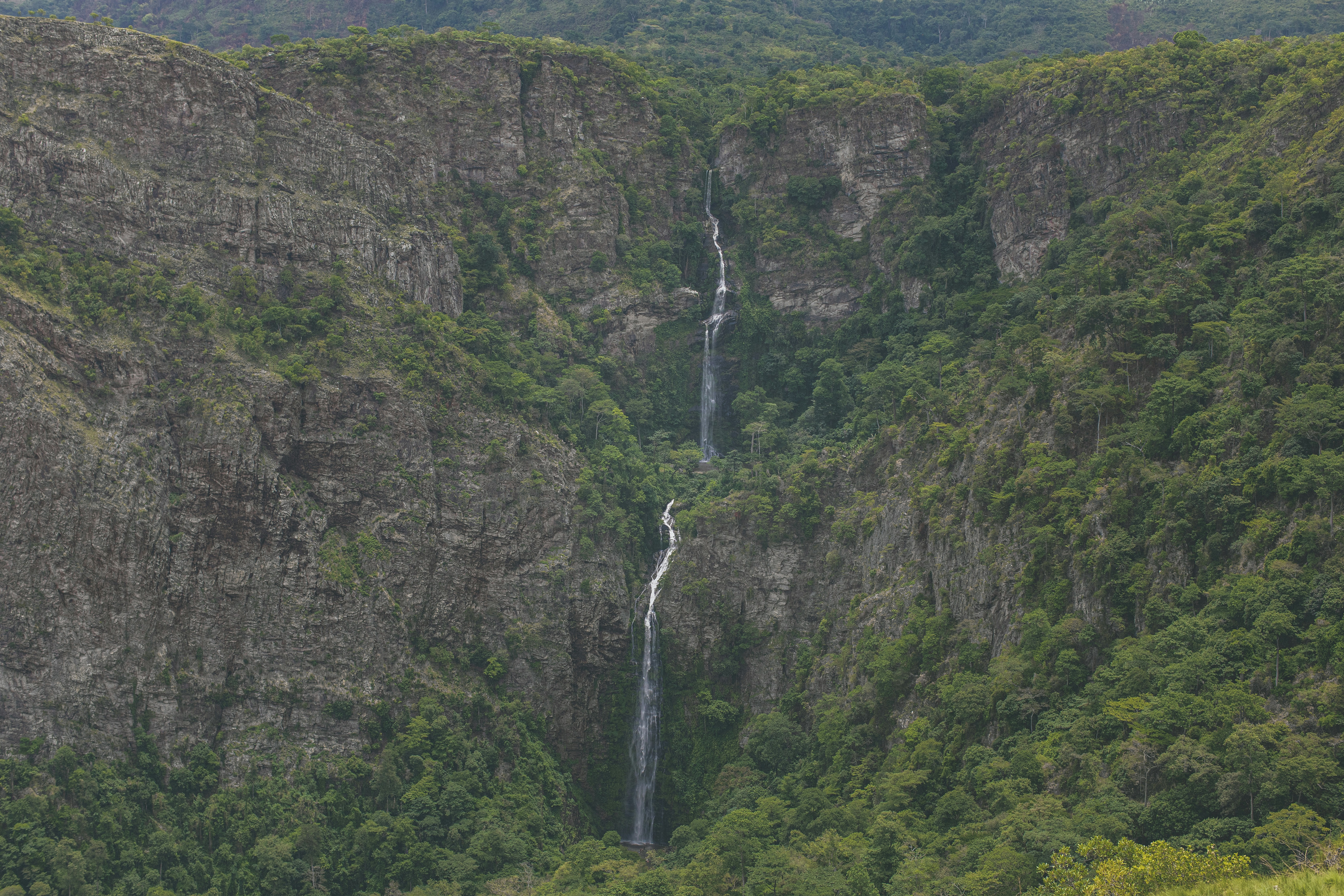 Twin waterfalls cascading down rocky cliffs into pool surrounded by tropical vegetation