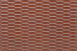 A rust-colored metal surface with a repeating pattern of raised, rectangular shapes aligned in parallel rows. The texture creates a rugged and industrial look.
