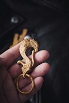 A hand is holding an intricately designed golden keychain shaped like a bird with detailed feather carvings.