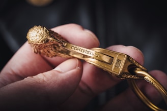 A close-up of a hand holding a metallic object resembling a carabiner, intricately designed to look like a bird with detailed feathers and features. The metal is golden in color and inscribed with the text 'COPPERTIST.WU'. The object's craftsmanship is highlighted by the focus and lighting.