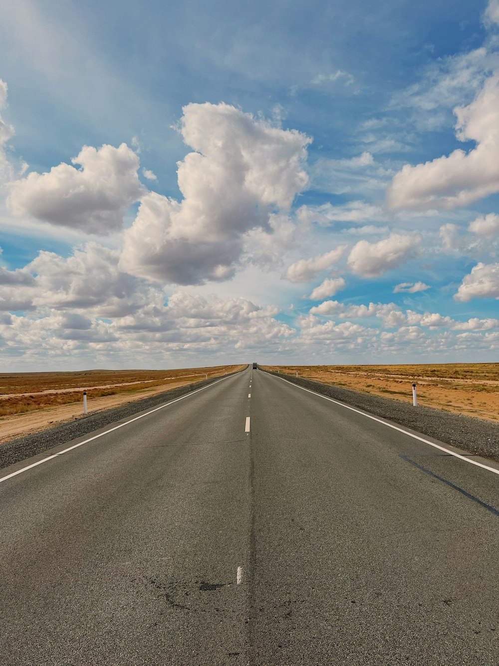 a long empty road with a sky filled with clouds