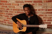 Geraal Love sitting quietly with a guitar, reflecting the calm and soulful vibe of his music.